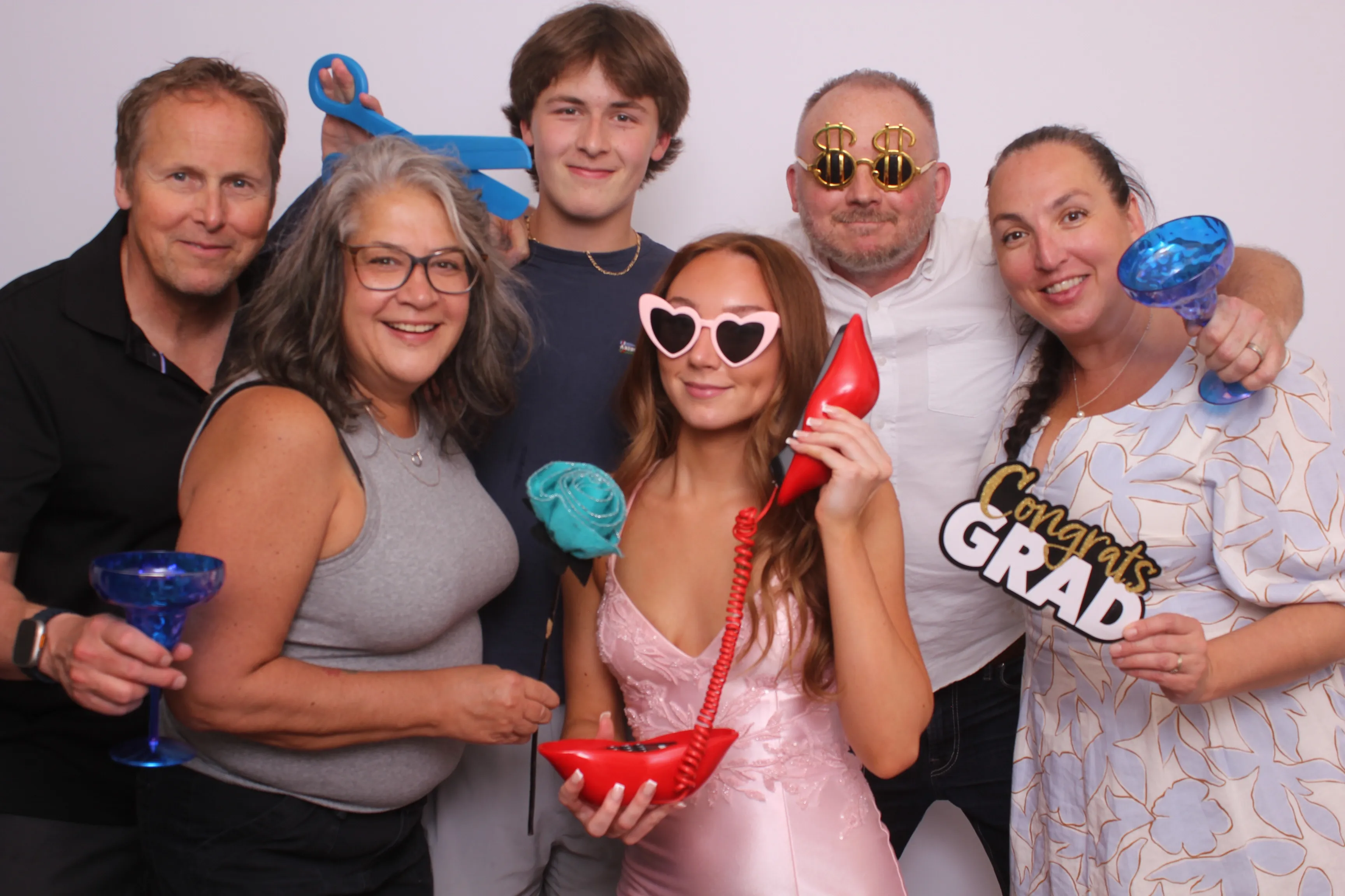 A family celebrating a graduation together, holding props including a 'Congrats GRAD' sign